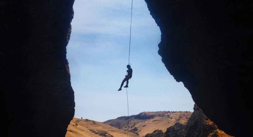 the silhouette of a rock climber on a rope rests between two rock walls while rappelling 